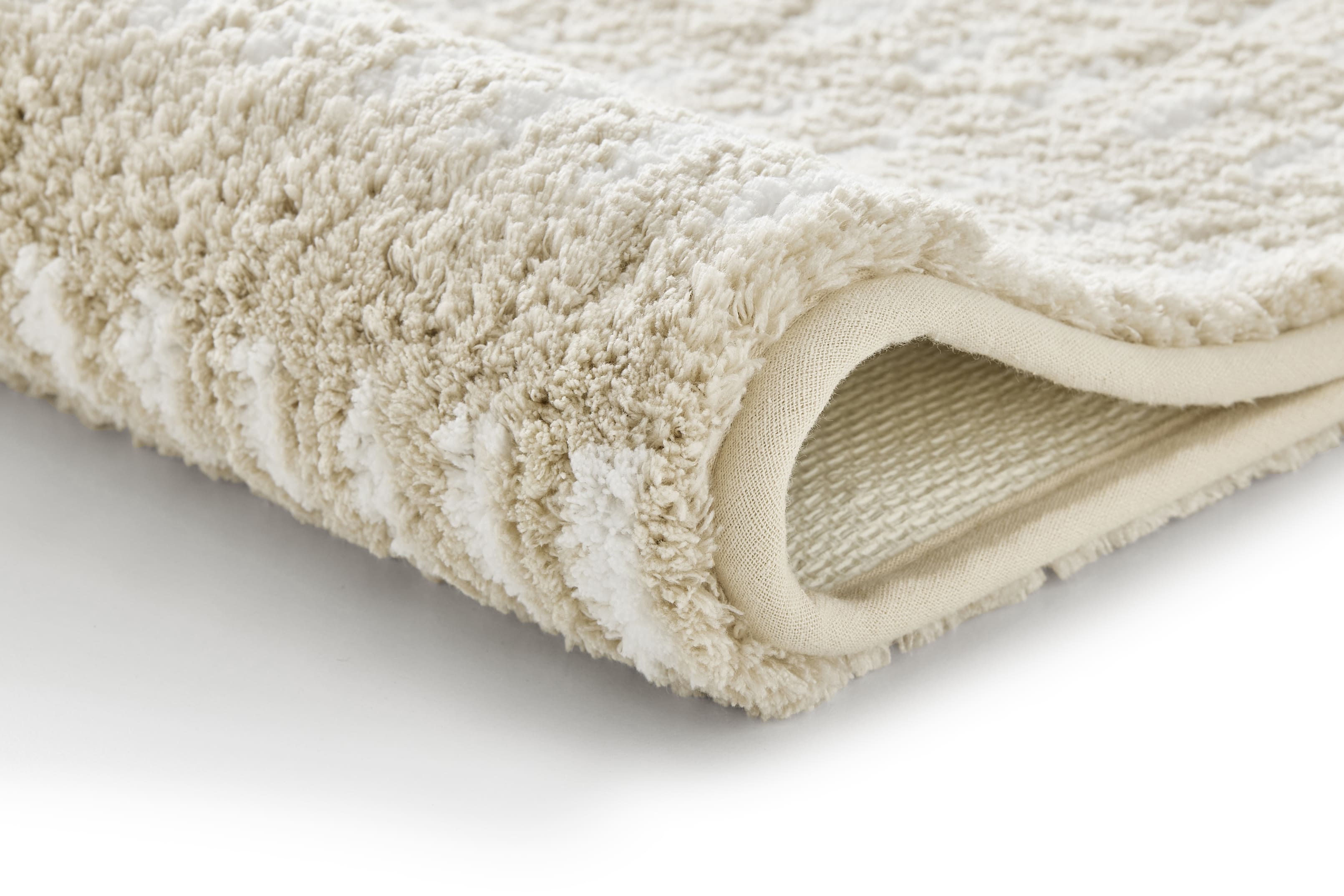 Weicher, beige-weißer Badteppich mit flauschiger Textur und rutschfester Unterseite, ideal für ein gemütliches Badezimmer.