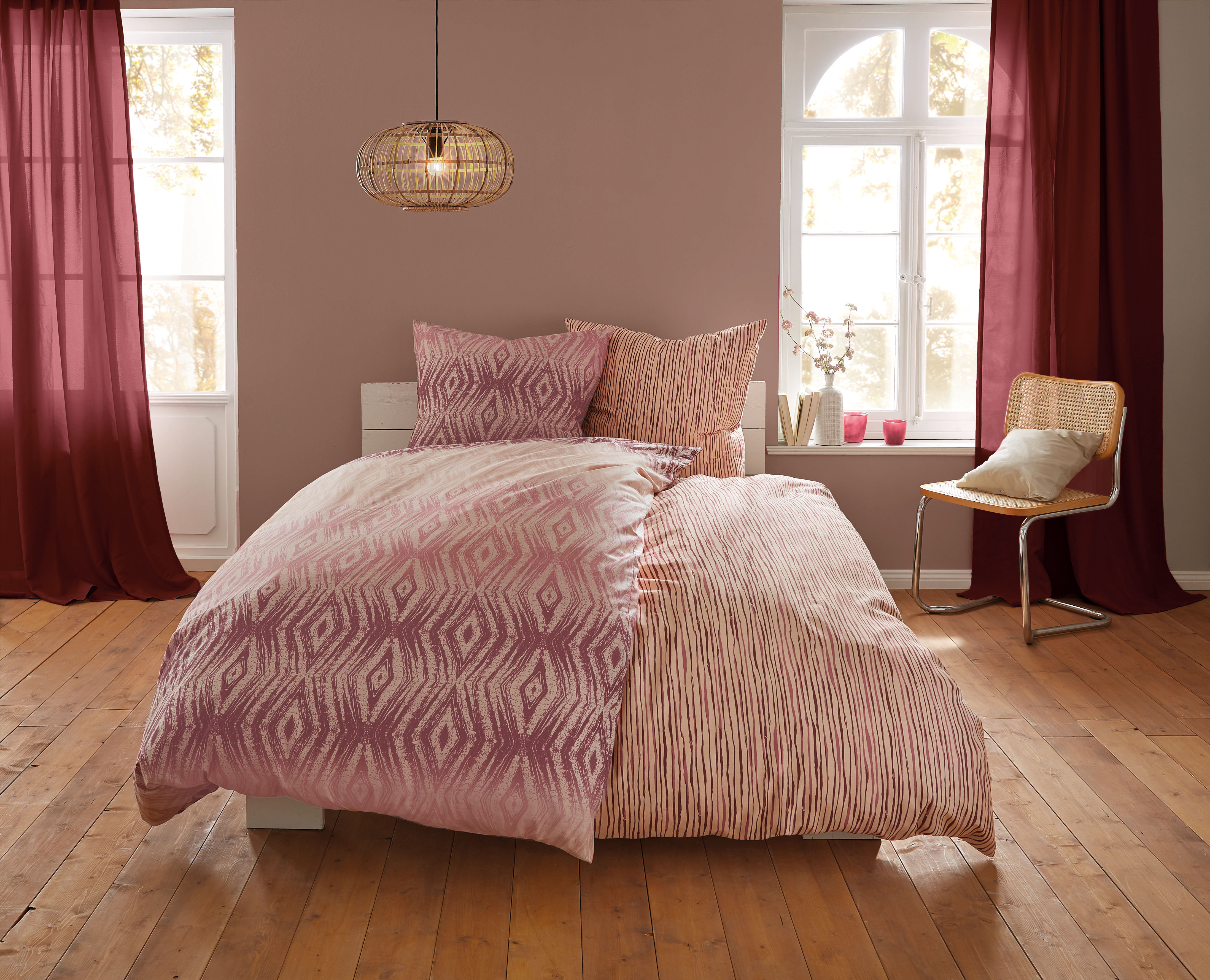 Bettwäsche-Set in Rosa mit geometrischem Muster, dekoriert in einem gemütlichen Schlafzimmer mit Holzboden und roten Vorhängen.