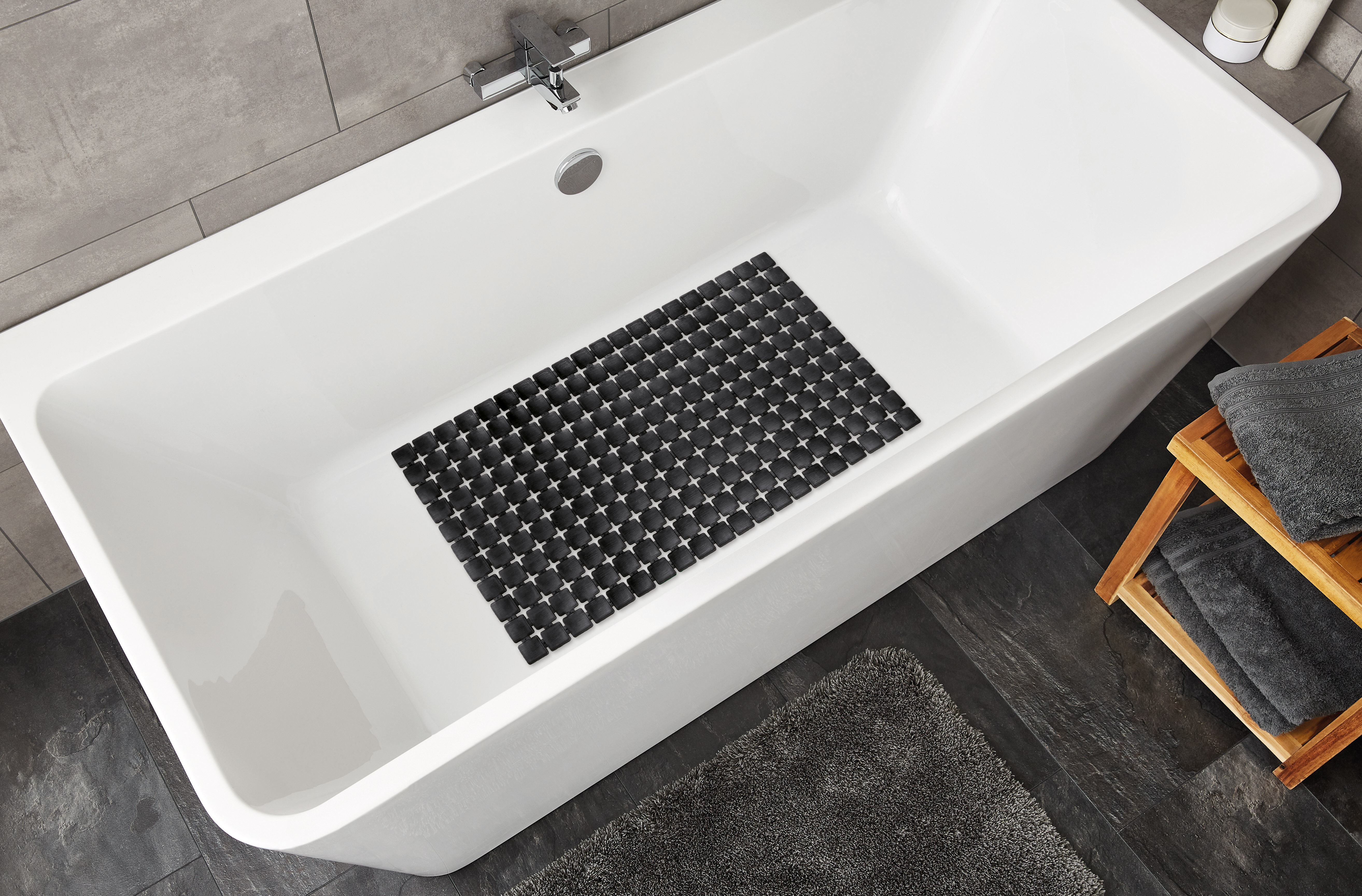 Rutschfeste schwarze Badematte mit geometrischem Muster in einer modernen weißen Badewanne, umgeben von grauen Handtüchern.