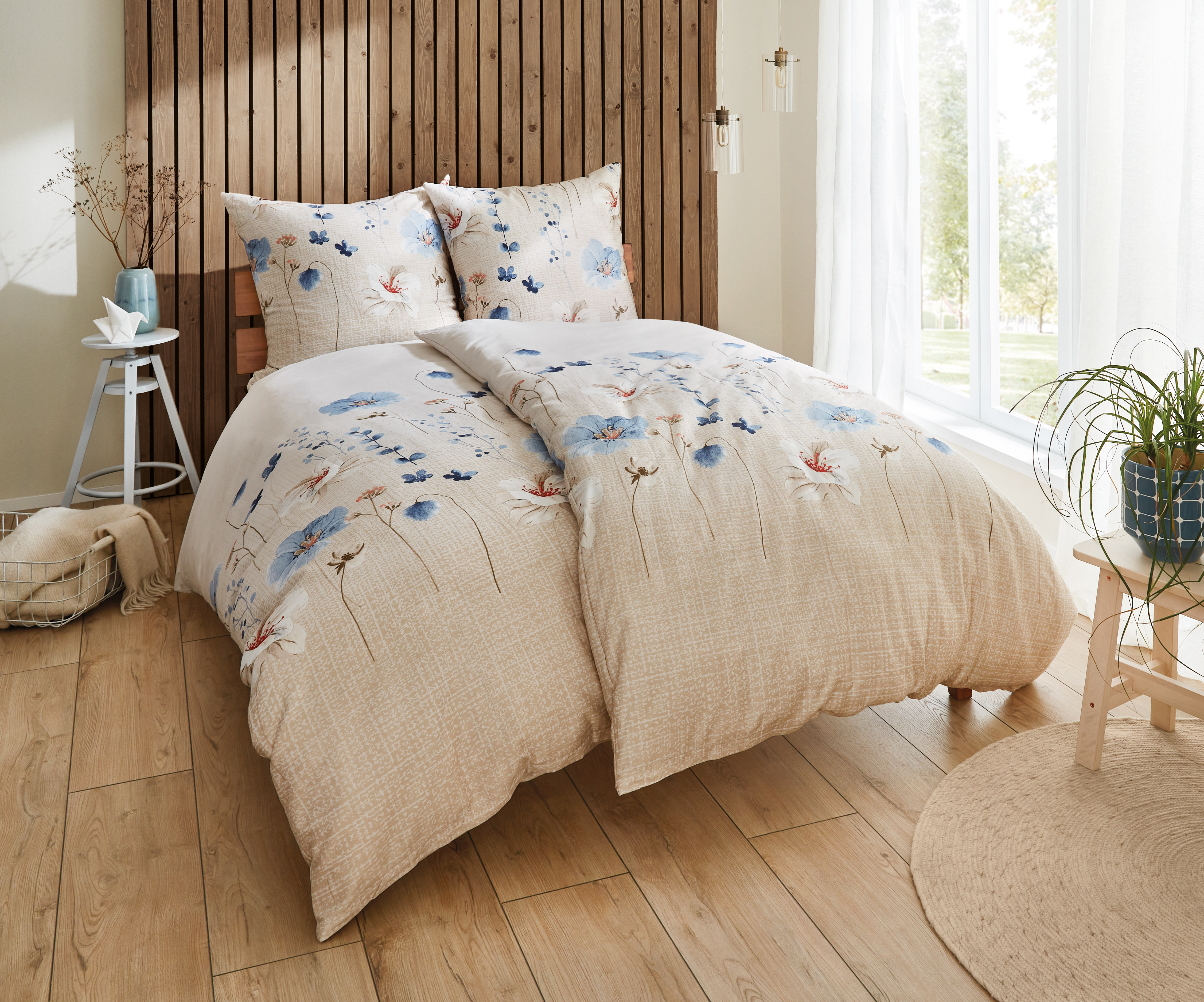 Bettwäsche-Set mit floralem Design in Beige und Blau, dekoriert mit Blumenmustern, auf einem gemütlichen Bett in einem hellen Raum.