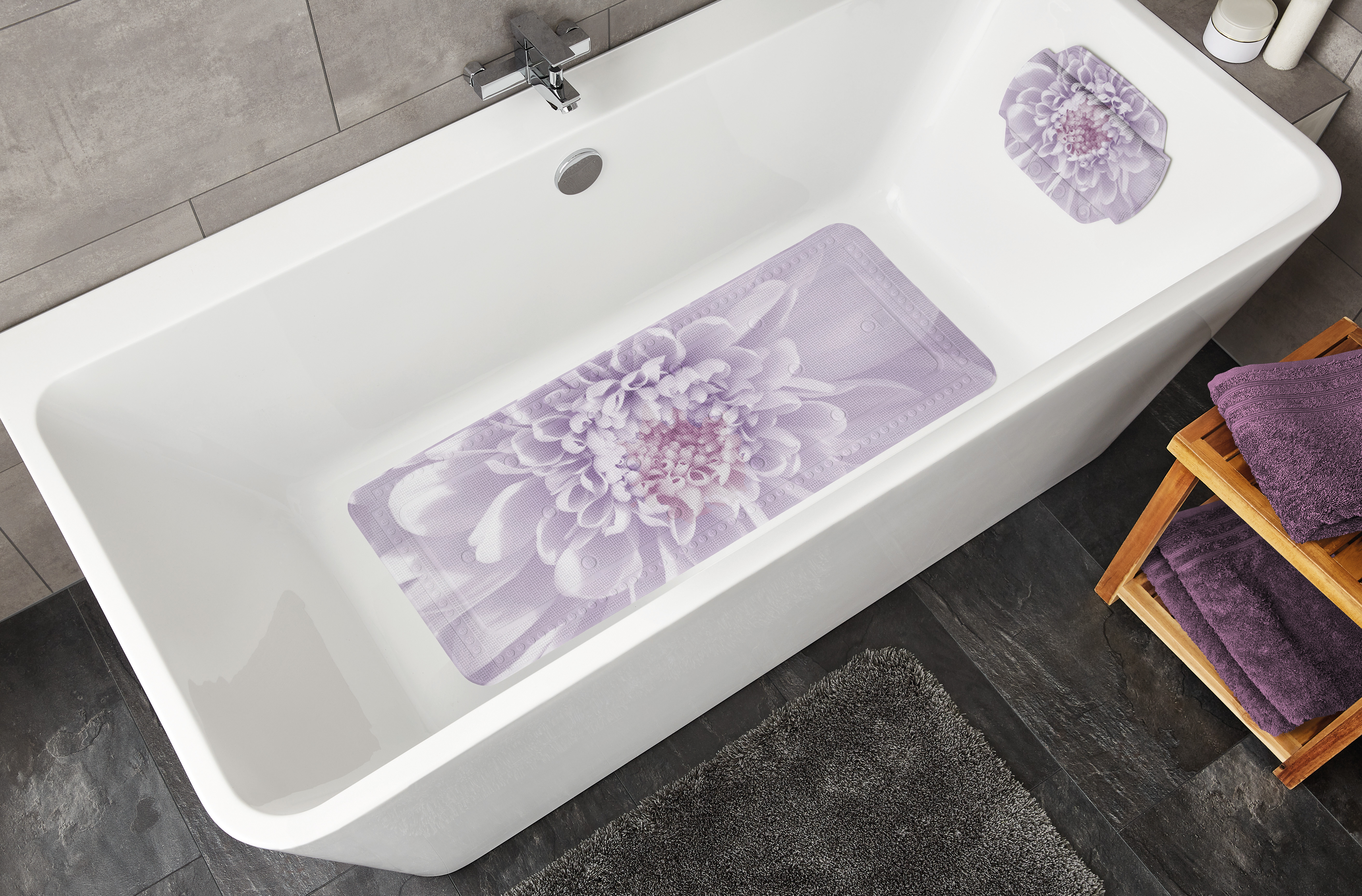 Rutschfeste Badematte und Nackenpolster in einer Badewanne, beide mit lila Blumenmuster, umgeben von modernen Badezimmer-Accessoires.