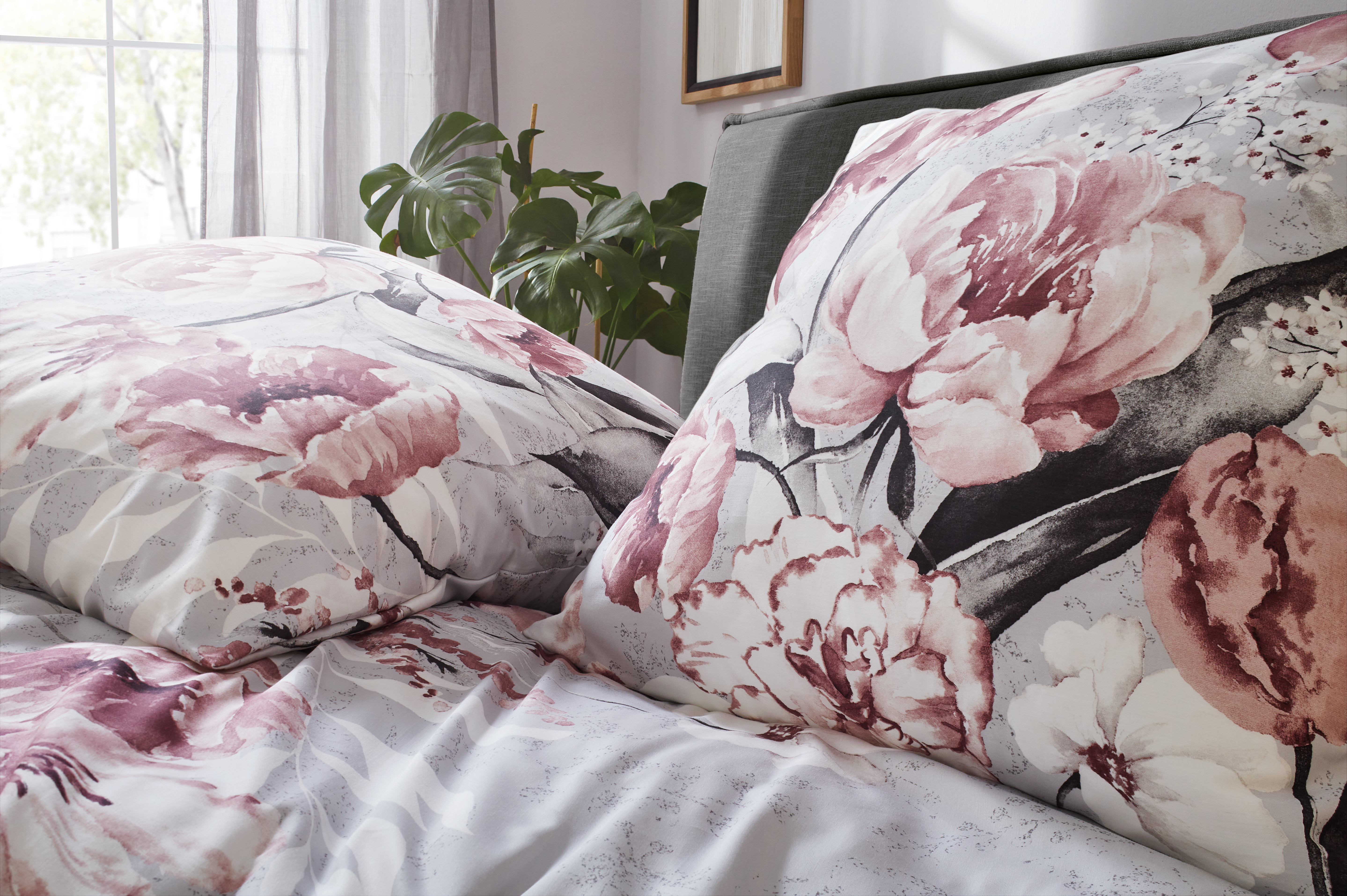 Bettwäsche-Set mit floralem Design in Rosa- und Grautönen, dekoriert mit großen Blumenmotiven, auf einem Bett arrangiert.